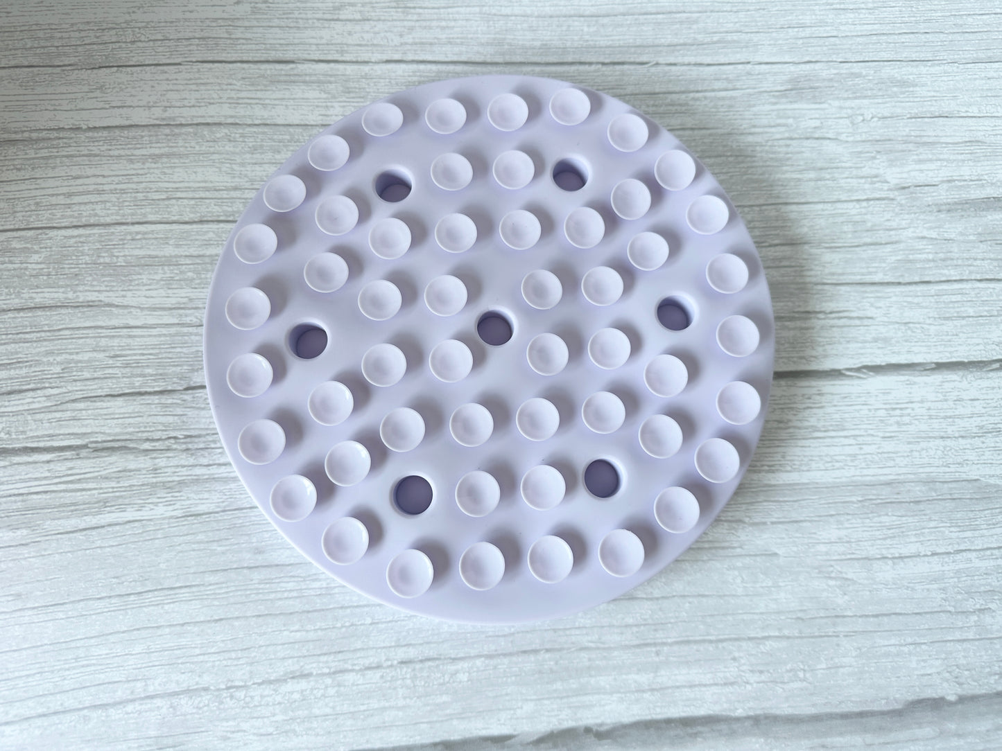 The Crafts by Kate Slow Feeder Pet Mat, a round white washable mat with suction cups, rests on light wood to ensure stability and promote better pet digestion during meals.