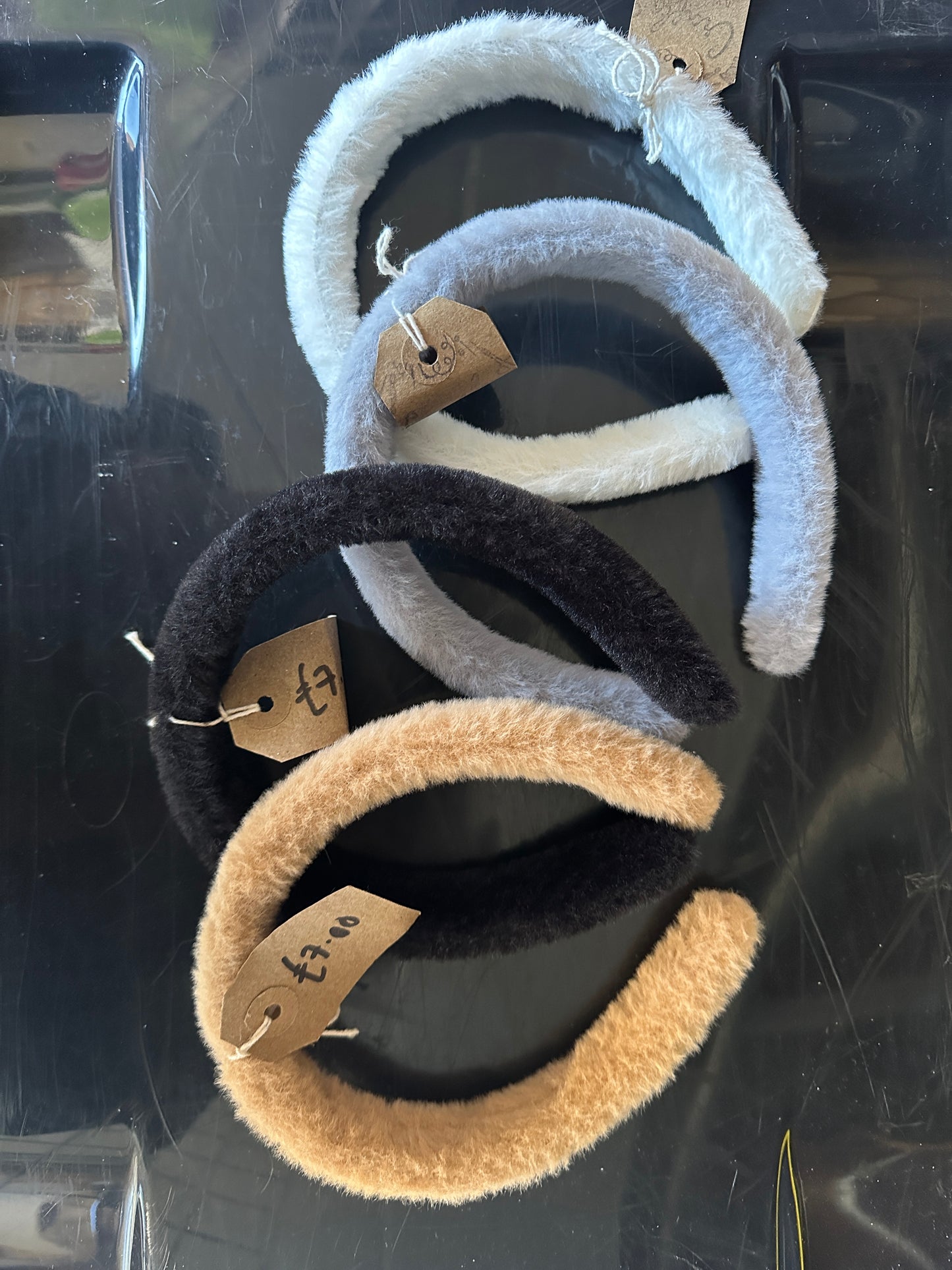 The "Custom Order - Fluffy Headbands" by Crafts by Kate features four fluffy headbands in light gray, beige, black, and blue-grey on a reflective black surface. Each has a small brown tag with "£7.50 each.