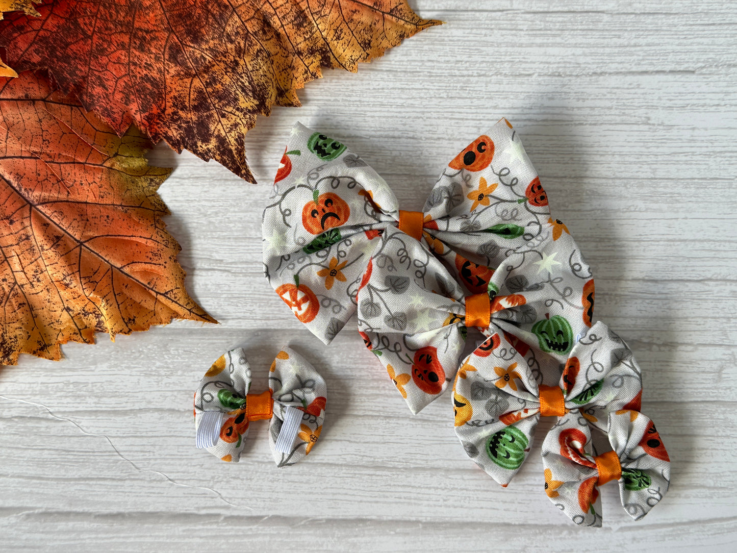 Three Crafts by Kate Cotton Pet Bows with glow-in-the-dark pumpkin designs, each with a collar attachment, are displayed on a light wooden surface—festive accessories for your furry friend.