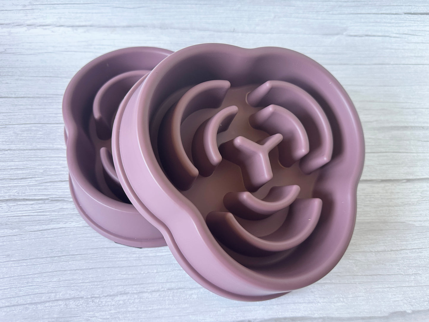 A pair of mauve silicone ice molds by Crafts by Kate, shaped like lion faces, rest on a light wooden surface. Resembling the Slow Feeder Pet Bowl, they feature detailed manes, eyes, and noses for a blend of fun and function.