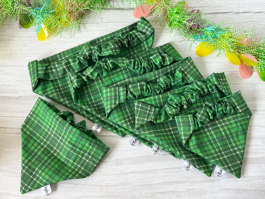 The Cotton Pet Scrunchie Bandanas - Bluey & Bingo by Crafts by Kate are displayed on a light wooden surface. Five bandanas form a cascading pattern, complemented by decorative greenery and colorful paper eggs in the background, showcasing their ruffled edges and spring tartan fabric.