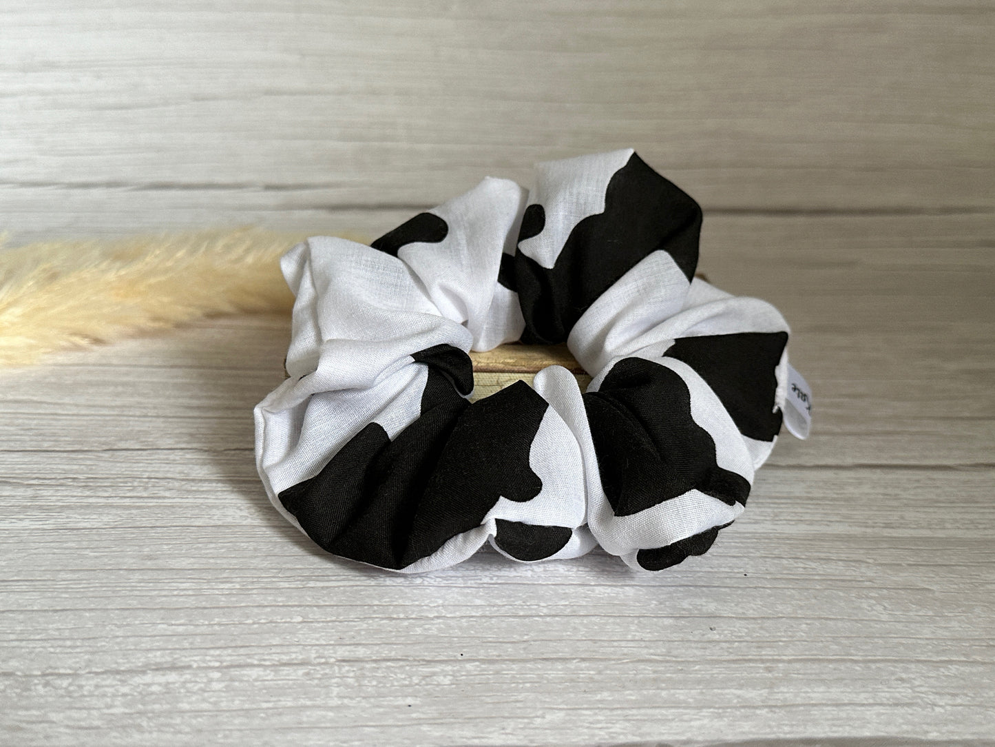 The "Cotton Extra Large Scrunchie - Cow Print" by Crafts by Kate is elegantly displayed on a light wooden surface.