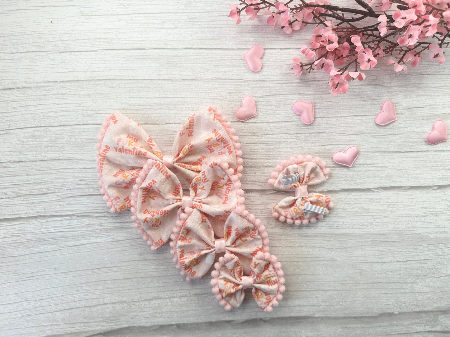 Crafts by Kate presents "My Fluffy Valentine," a cotton pet bow with collar attachment, elegantly displayed on white wood. This charming Valentine's Day piece features pink flowers and heart-shaped decorations, crafted from soft fabric for a delightful touch.