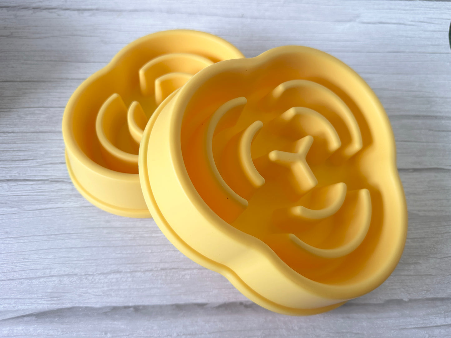 Two yellow, cloud-shaped silicone trivets with geometric grooves sit on a light wooden surface, echoing the playful design of the Crafts by Kate Slow Feeder Pet Bowl, known to promote better digestion.