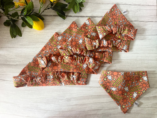 Four orange Cotton Pet Scrunchie Bandanas—"I’m a ray of f***ing sunshine" by Crafts by Kate—feature ruffles and paw prints. Displayed on light wood with lemons and green leaves, these handcrafted cotton accessories add playful charm for your pet.