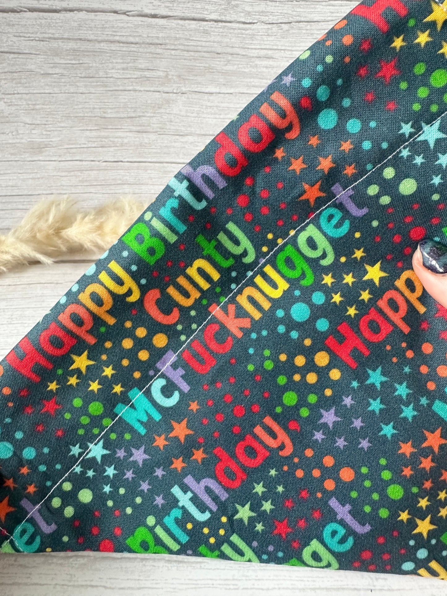 The Cotton Pet Bandana by Crafts by Kate showcases playful text "Happy Birthday C Mcnugget" amid multicolored dots, while a feather and painted nails slide through the collar for added charm.