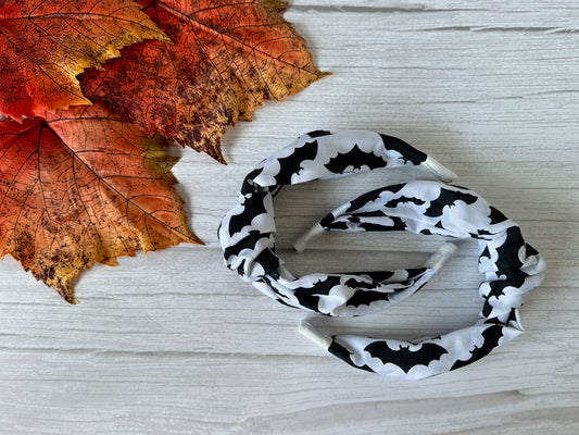 The Cotton Knotted Headband - Bats by Crafts by Kate is shown on a white wooden surface beside orange and red autumn leaves.