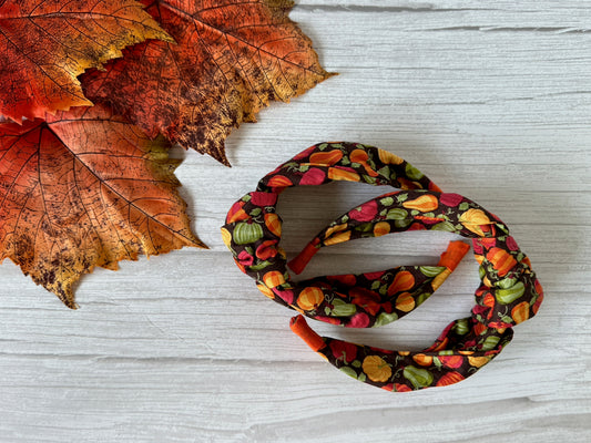 Three Crafts by Kate Cotton Knotted Headbands in the Pumpkin Lovers design rest on a white wooden surface, accented with artificial orange and red fall leaves.