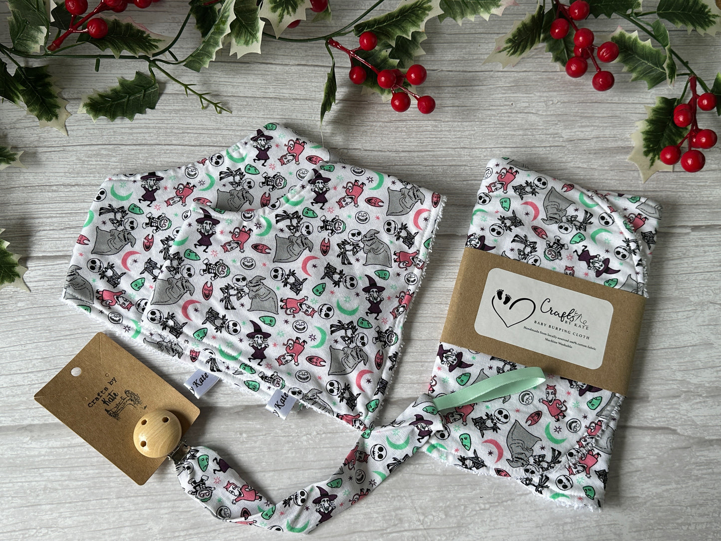 Crafts by Kate presents Cotton & Terry Towelling Baby Sets—Nightmare Before Christmas—displayed on a light wooden surface with festive holly and berry decorations. A label reads "Handmade With Love.