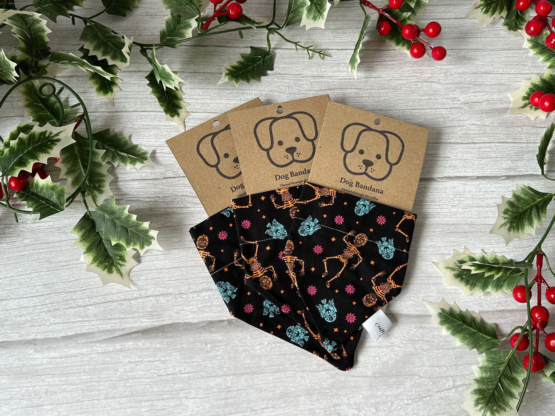 Three handcrafted black cotton pet bandanas by Crafts by Kate, featuring Star Wars Christmas designs and collar attachments, are displayed on a white wooden surface with festive holly and red berries. Each is attached to a brown card with a dog illustration.