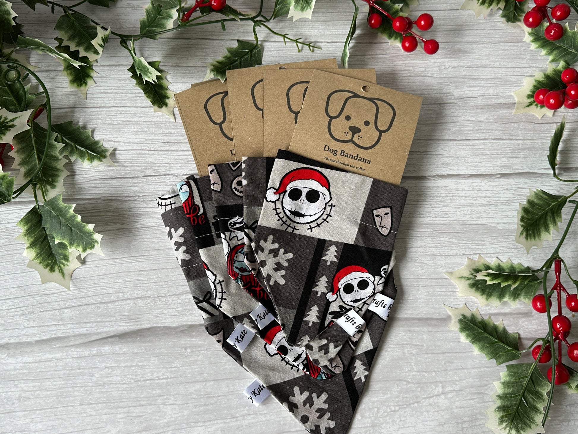 Four handcrafted Crafts by Kate Cotton Pet Bandanas with collar attachment, featuring Jack Skeleton’s Christmas cartoon faces and snowflakes. Each comes with a brown “Dog Bandana” label showing a dog’s face, holly, and berries on light wood.