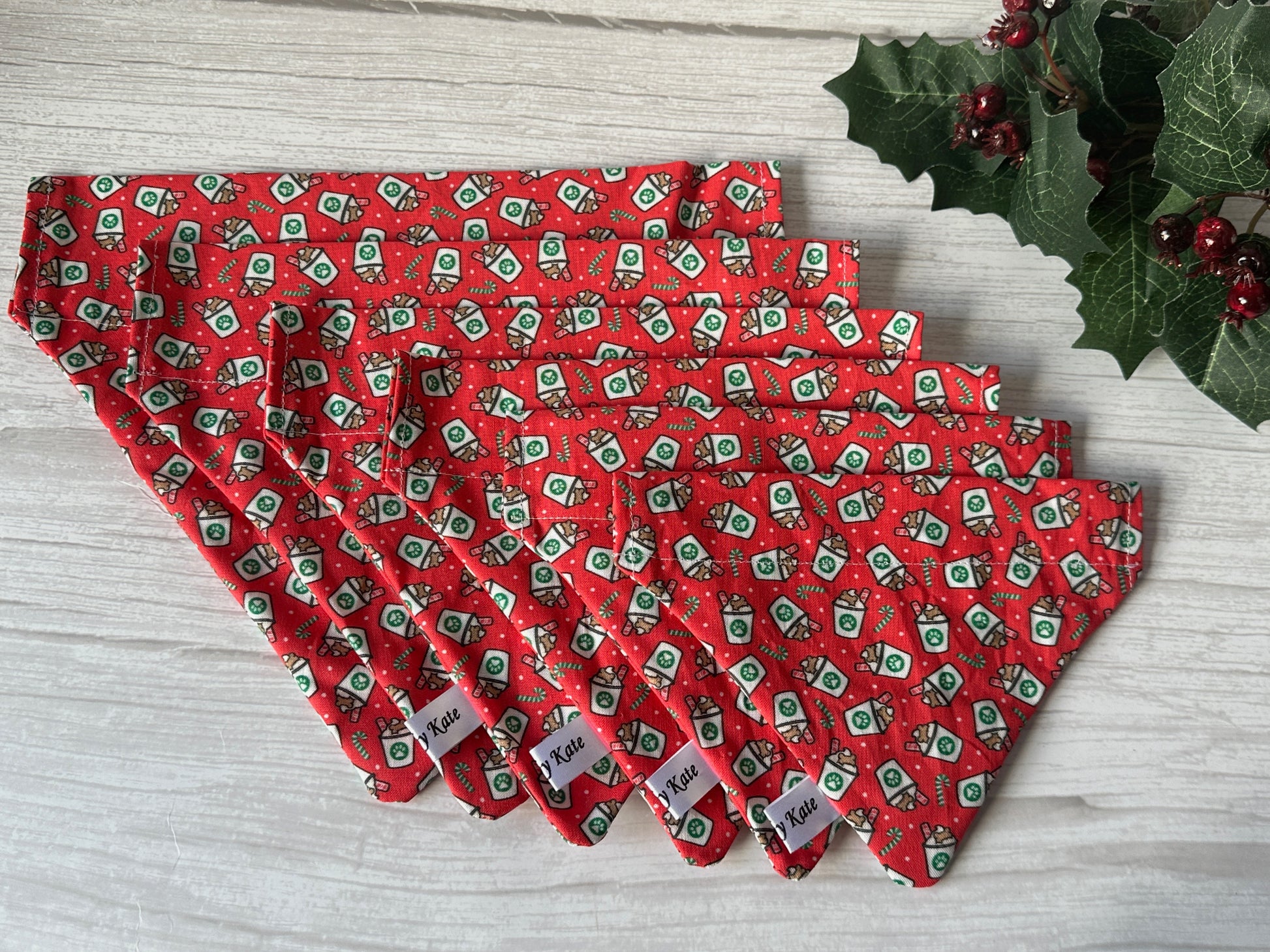 Six handcrafted red “Christmas Pupcup” Cotton Pet Bandanas with collar attachments by Crafts by Kate, featuring festive green and white prints, are displayed on light wood with holly—ideal “1-4L” holiday accessories for your pup.