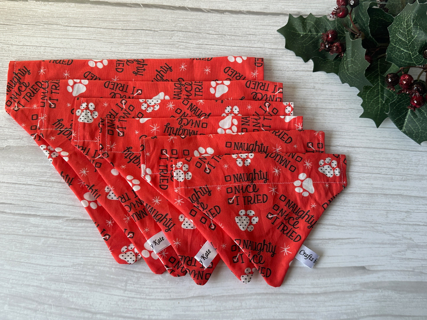 The "I Tried" Cotton Pet Bandana with collar attachment by Crafts by Kate is displayed on a white wooden surface, featuring red fabric with white paw prints, snowflakes, and playful holiday text, accented by decorative holly.