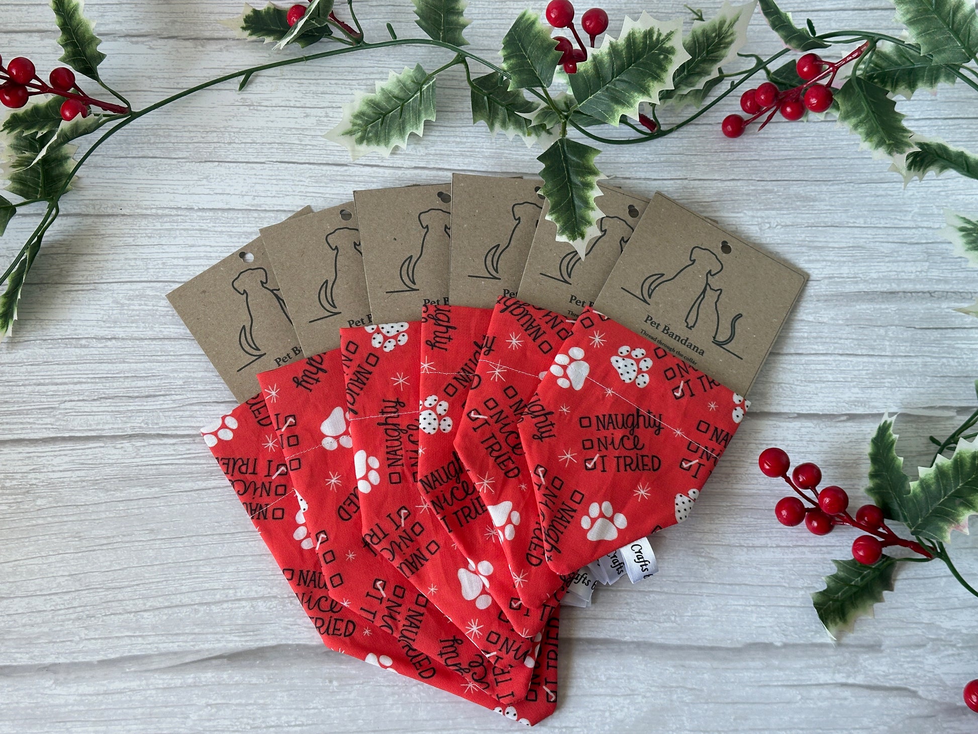 Six Crafts by Kate Cotton Pet Bandanas with collar attachment, featuring "I Tried" text and white paw prints, are fanned out on a light wood surface with holly leaves and red berries for decoration.