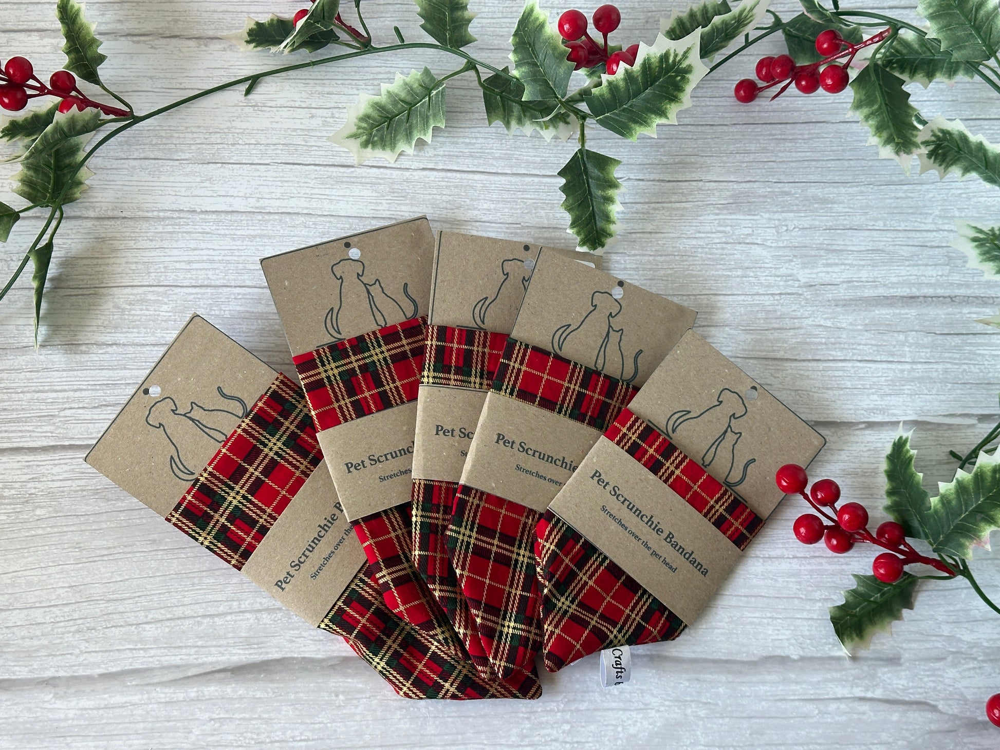 Five Crafts by Kate Cotton Pet Scrunchie Bandanas - Red & Gold Tartan are arranged in a fan shape on white wood, packaged in brown and accented with festive holly leaves and red berries.