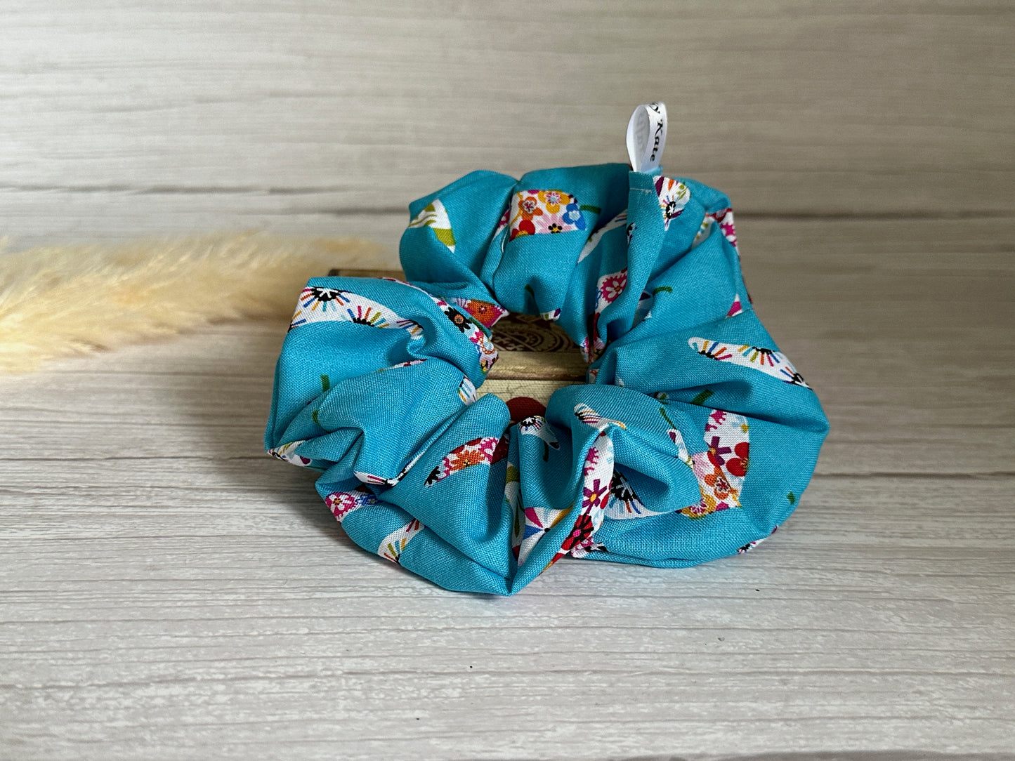 The Cotton Extra Large Scrunchie - Summer Chilli by Crafts by Kate, featuring vibrant multicolored floral patterns, is elegantly displayed on a light wooden surface.