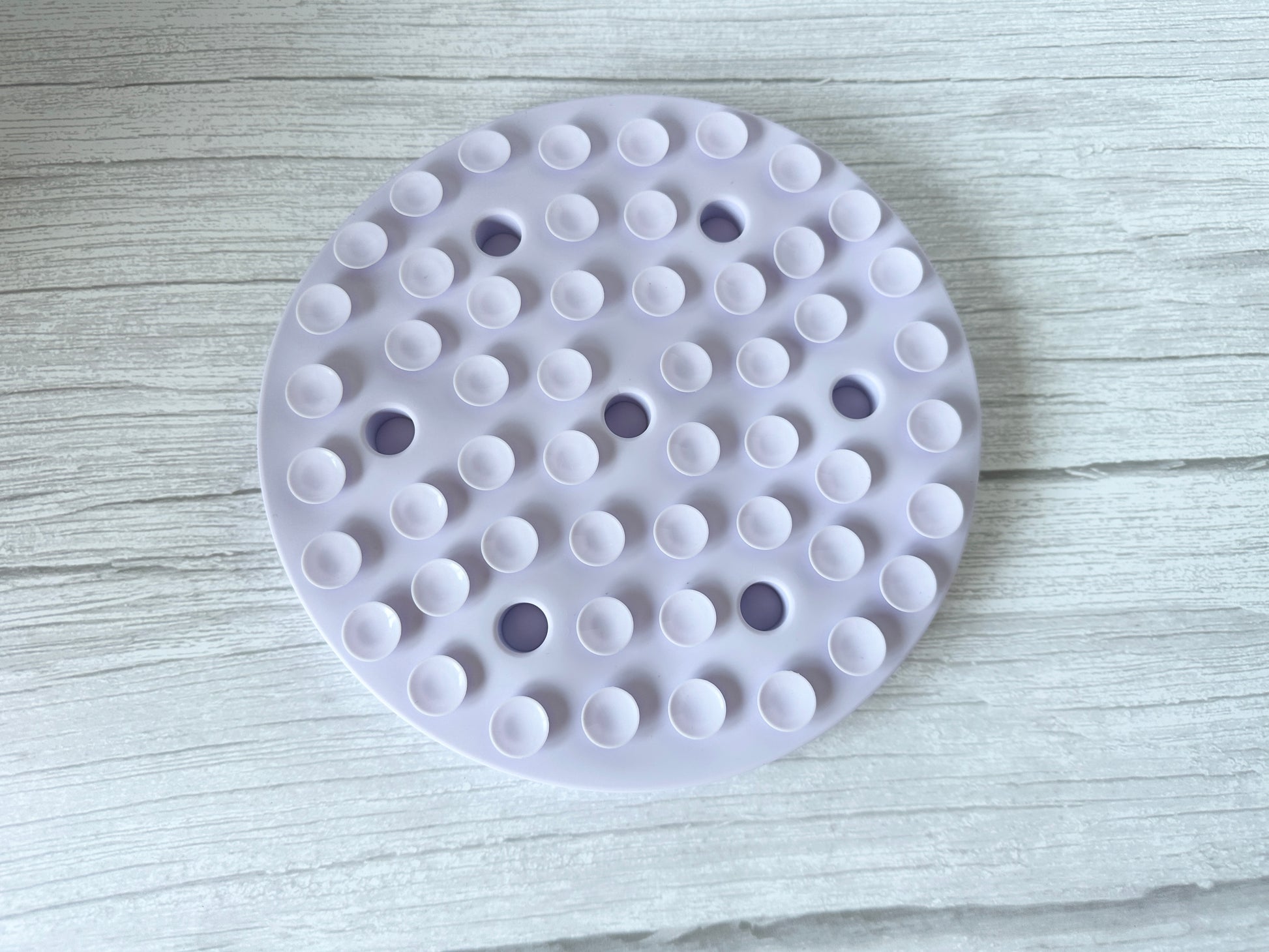 The Crafts by Kate Slow Feeder Pet Mat, a round white washable mat with suction cups, rests on light wood to ensure stability and promote better pet digestion during meals.