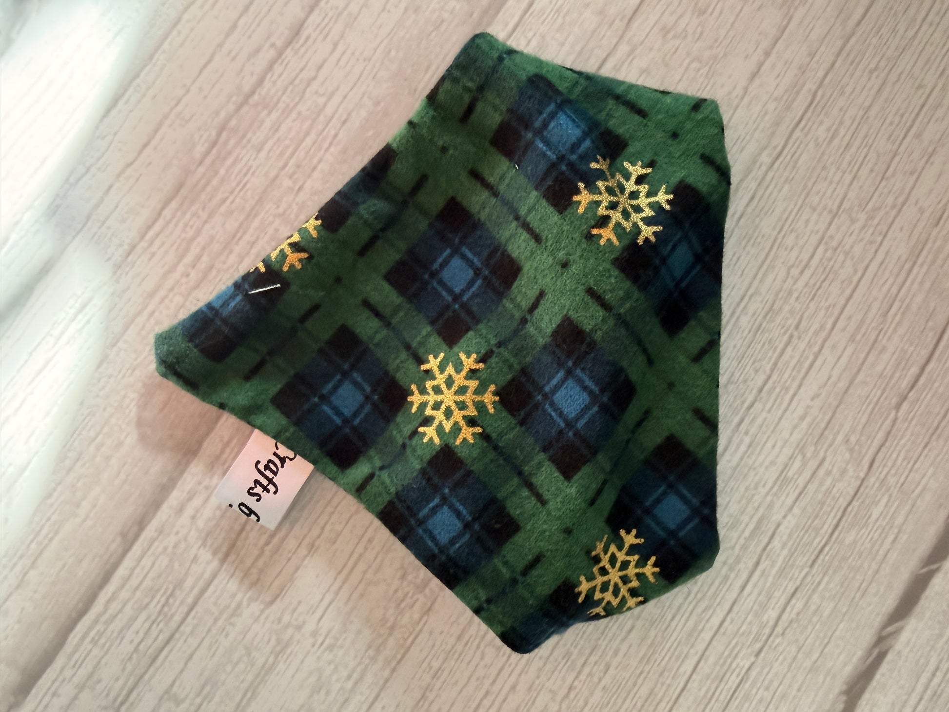 A Custom Order - AGL photography face mask by Crafts by Kate with green and blue plaid and yellow snowflakes rests on light wood, featuring a white side tag with black writing.
