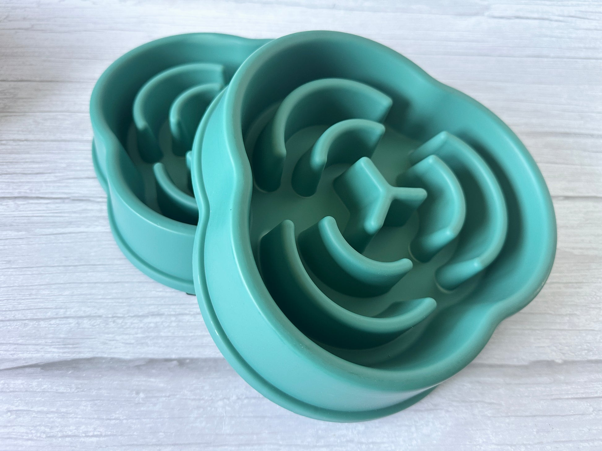 Two teal silicone Crafts by Kate Slow Feeder Pet Bowls with a spiral design for better digestion sit on a white wooden surface. These washable bowls are both functional and stylish.