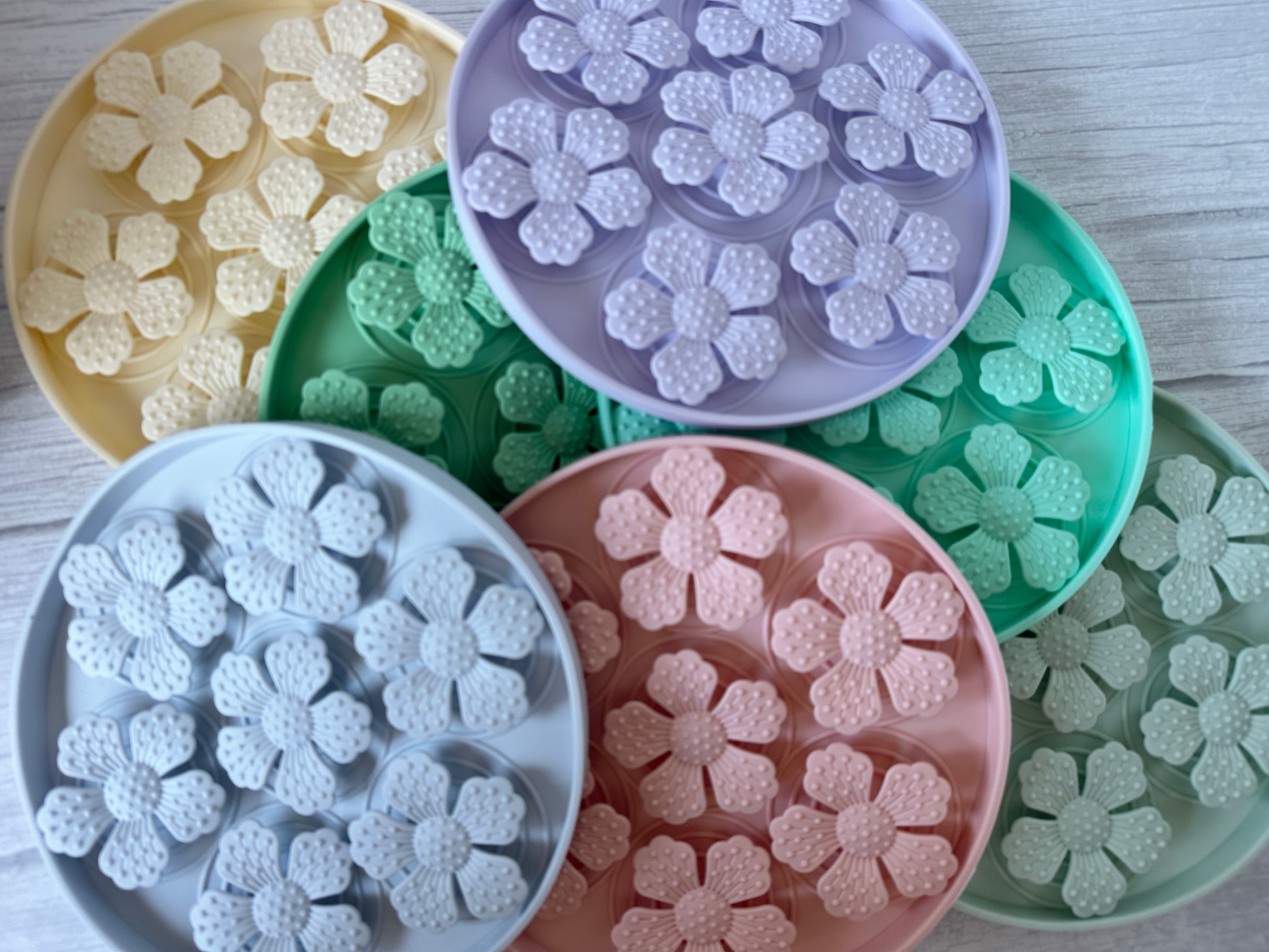 Crafts by Kate's Slow Feeder Pet Mat features round pastel containers with floral patterns and five flower-shaped compartments, resting on a light wooden surface. Versatile and washable, this mat enhances pet digestion while adding a cheerful touch to any space.