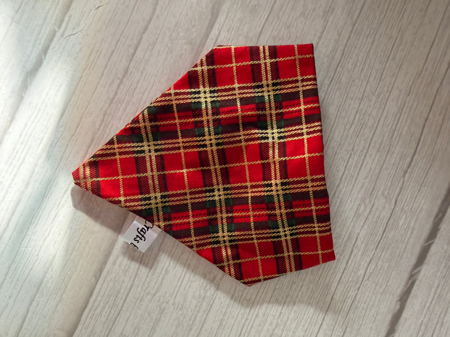 A Custom Order - AGL photography scrunchie bandana by Crafts by Kate, featuring red plaid with yellow, black, and white stripes, sits on a light wood surface. A small white tag with black writing is attached.