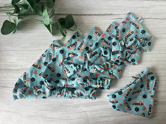 The image shows four blue, patterned fabric bonnets with "favorite child," hearts, and paw prints, beside a green plant—ideal for pairing with the Crafts by Kate Cotton Pet Scrunchie Bandana - Favourite Child.