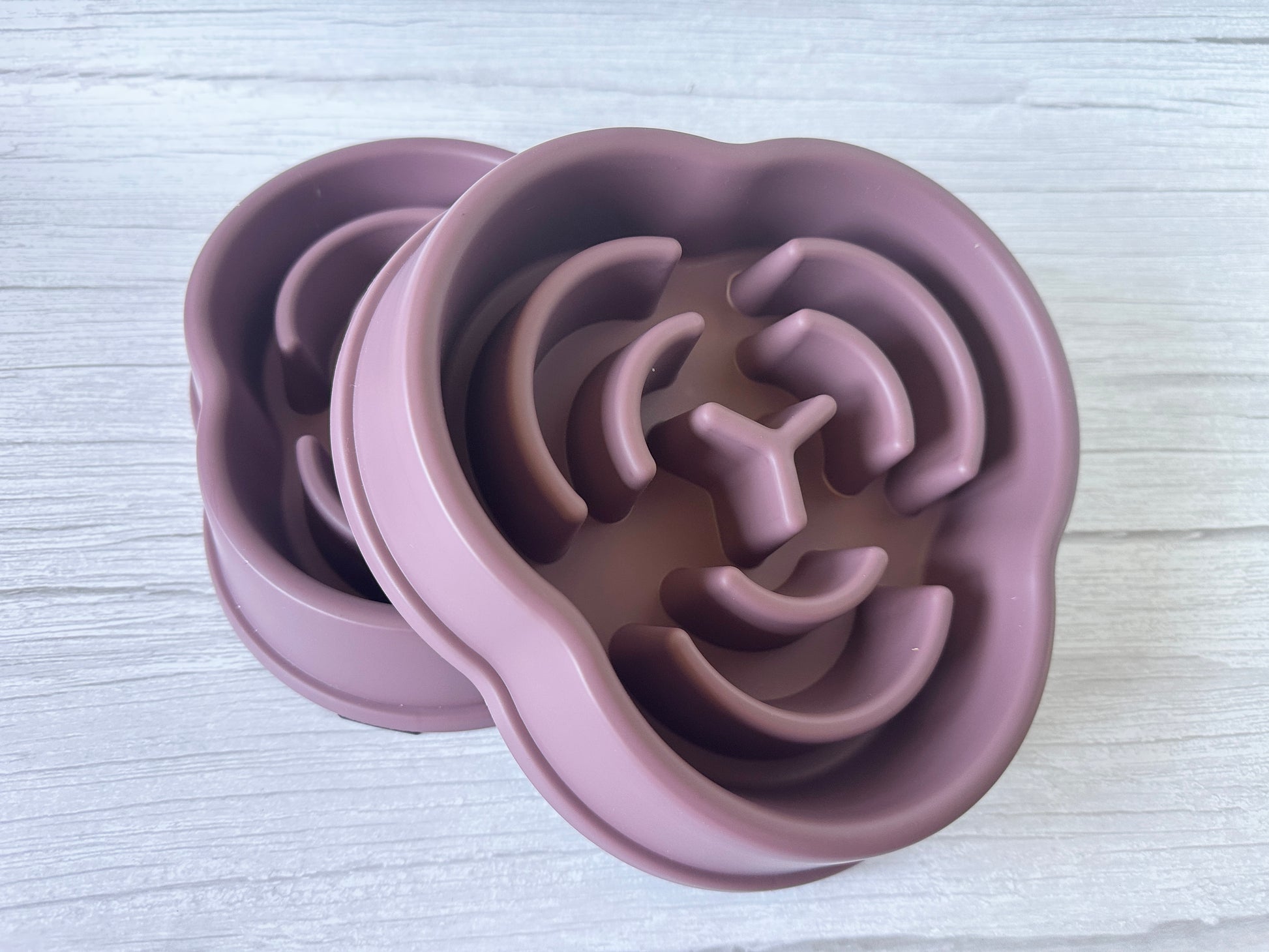 A pair of mauve silicone ice molds by Crafts by Kate, shaped like lion faces, rest on a light wooden surface. Resembling the Slow Feeder Pet Bowl, they feature detailed manes, eyes, and noses for a blend of fun and function.