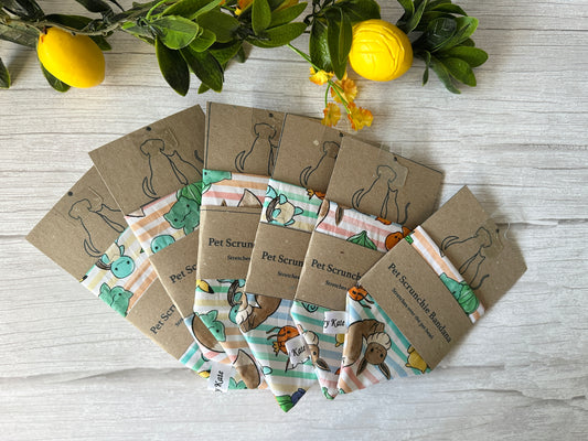 A fan arrangement of six colorful Crafts by Kate Cotton Pet Scrunchie Bandana - Pokemon designs, each on a brown card with an illustrated dog, bordered at the top by green leaves and yellow lemons.