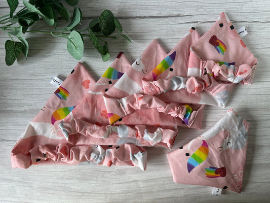 The Crafts by Kate Cotton Pet Scrunchie Bandana - Bitch I’m a Unicorn, featuring pink fabric with rainbow and heart patterns, is displayed on light wood with a small green plant adding charm to this LGBTIQA+ pet accessory setup.