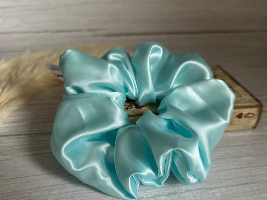 An extravagant Silk Extra Large Scrunchie - Aqua Blue by Crafts by Kate graces a wooden surface. Positioned behind it is a rectangular decorative box with delicate patterns, complemented by a tuft of beige pampas grass on the left.