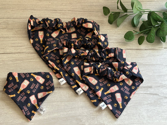 Crafts by Kate presents the Cotton Pet Scrunchie Bandana - Nosé all day, featuring "Rose All Day" and champagne bottle prints on black. Perfect for Gotcha Day celebrations, these chic accessories are elegantly displayed on light wood with a small green plant.