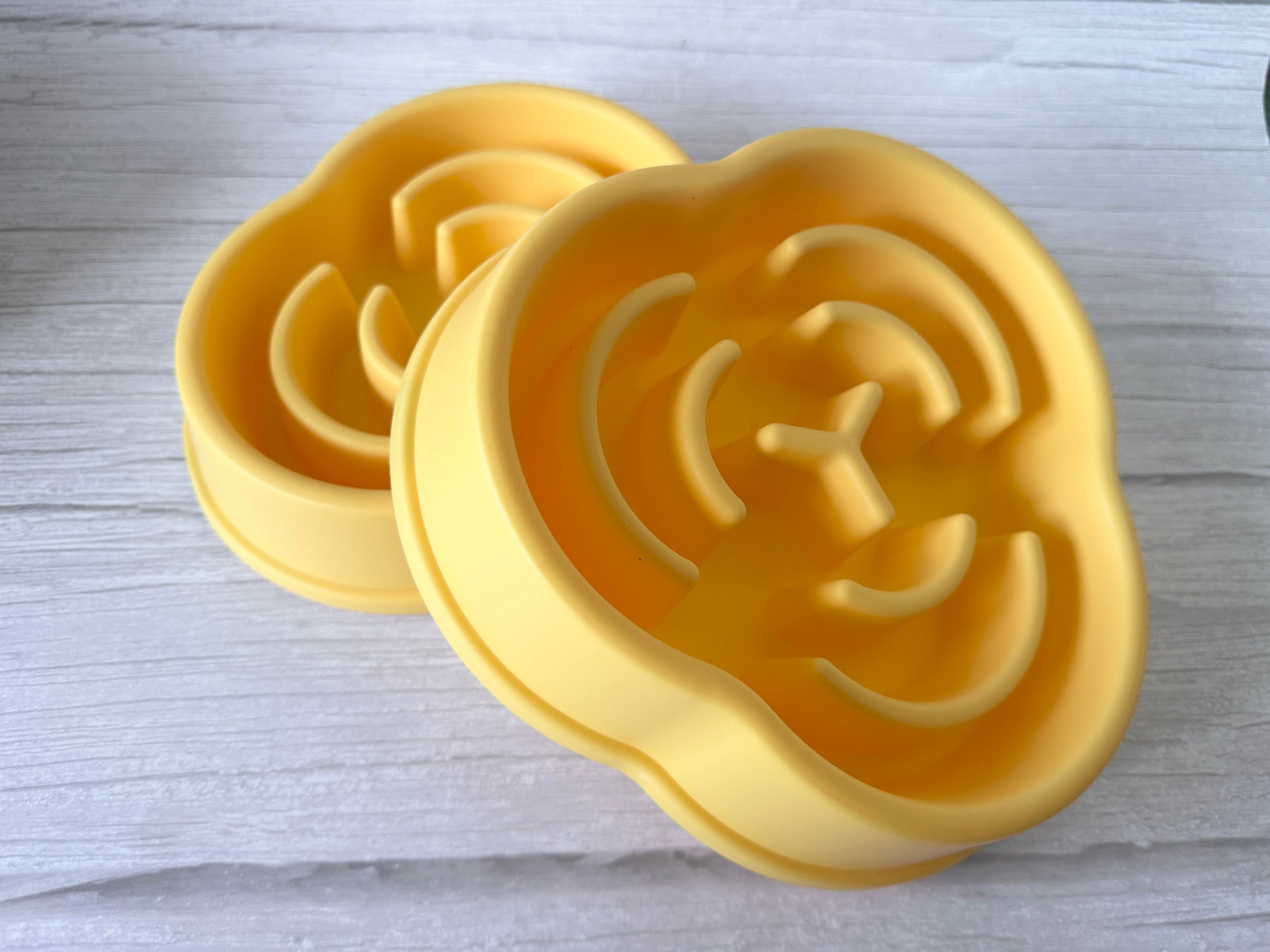Two yellow, cloud-shaped silicone trivets with geometric grooves sit on a light wooden surface, echoing the playful design of the Crafts by Kate Slow Feeder Pet Bowl, known to promote better digestion.