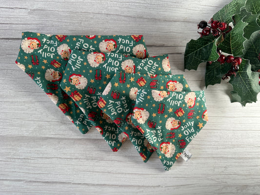 Crafts by Kate's "Jolly Old F***" cotton pet scrunchie bandana adds charm beside festive cloth napkins with Santa faces and gifts, all arranged on a light wooden surface. A holly branch with red berries enhances the display in the top right corner.