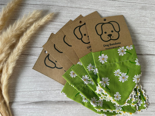 Four Crafts by Kate Cotton Pet Bandanas with collar attachments, green with white daisy patterns, are displayed alongside decorative wheat stalks on a light wooden surface. Handcrafted from premium cotton fabric, each bandana comes attached to a brown cardboard tag featuring a simple dog face illustration and the text "Dog Bandana.