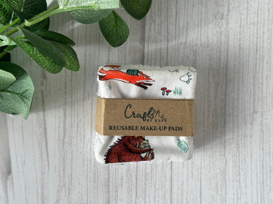 A stack of Cotton Reusable Make-up Remover Pads - Gruffalo in the Forest, wrapped in a brown paper band with the brand name "Crafts by Kate" printed on it. The pads feature a white background adorned with illustrations of forest animals such as a fox and a bear. Green leaves are partially visible to the left, emphasizing their environmentally friendly design.