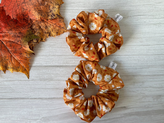 Two Crafts by Kate Cotton Extra Large Scrunchies in autumn florals rest on a light wooden surface with dried leaves, creating a lovely fall display. Small tags adorn these luxury scrunchies, adding an elegant touch to the seasonal arrangement.