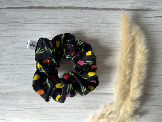 The Crafts by Kate Cotton Extra Large Scrunchie in a vibrant tulip print is elegantly displayed on a light wooden surface, accompanied by two feathery pampas grass stalks.