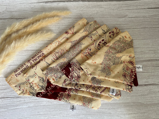 Cotton pet bandanas with collar attachments, featuring a beige and reddish-brown design reminiscent of Harry Potter's Marauders Map by Crafts by Kate, are neatly arranged on a light wooden surface. To the left, a few strands of beige pampas grass add a decorative touch.